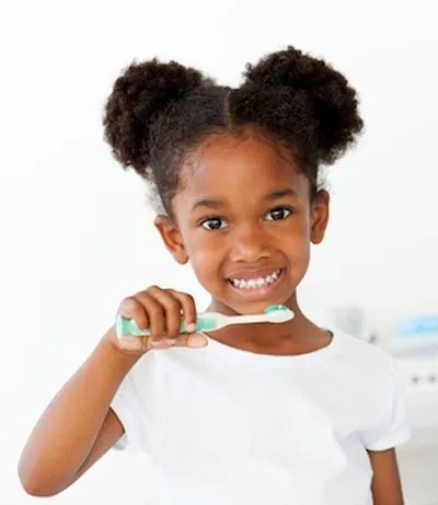 young girl smiling while brushing her teeth